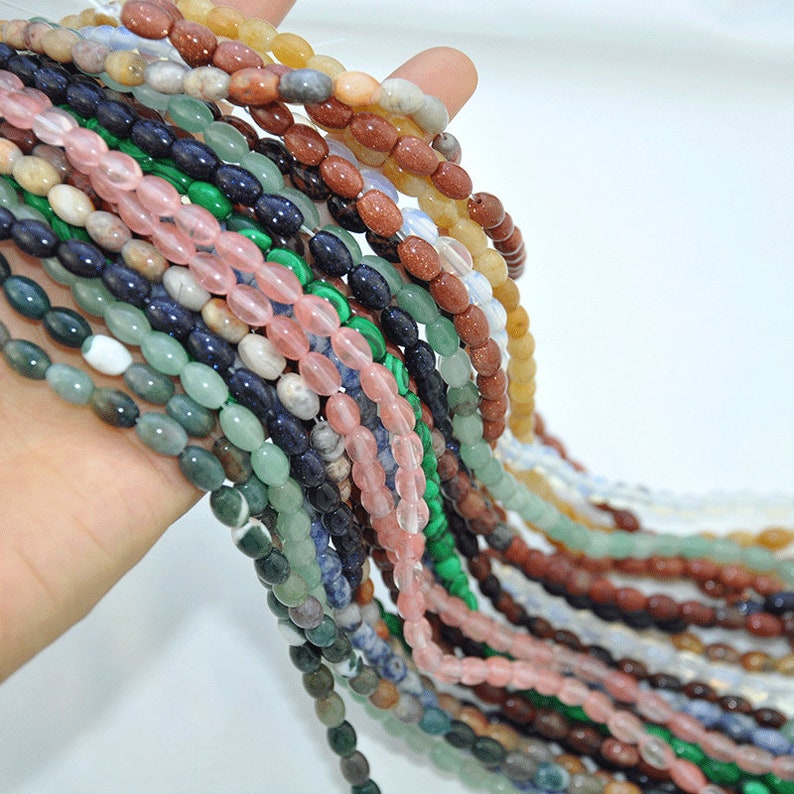 Pu&ograve; includere: Un filo di perline ovali in pietre preziose di vari colori, tra cui verde, blu, rosa, marrone e bianco. Le perline sono infilate su un filo trasparente e sono disposte a cascata.