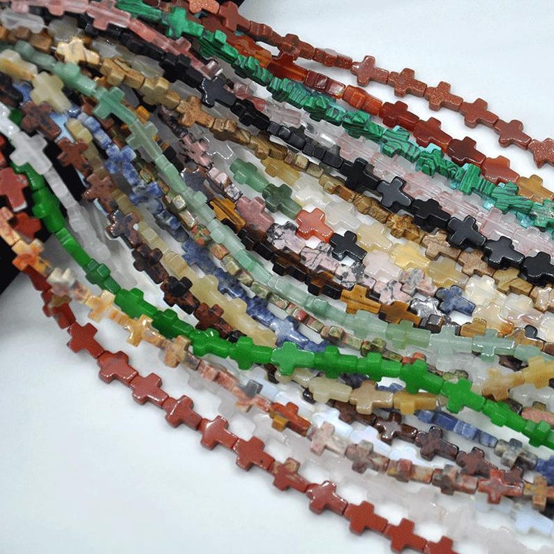 May include: A strand of colorful gemstone cross beads. The beads are made of various stones, including green, red, brown, and white. The cross shape is a popular design for jewelry making.
