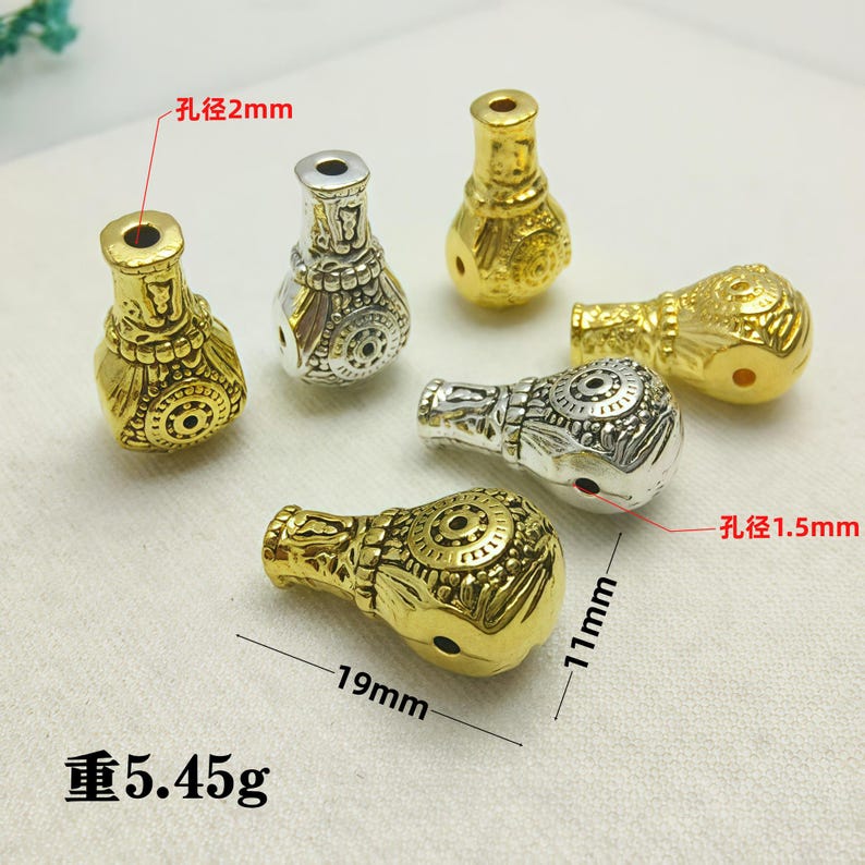May include: An assortment of decorative beads in gold and silver tones. The beads are approximately 19mm long and 11mm wide, with a weight of 5.45 grams. The hole diameter is 2mm and 1.5mm. The beads have an ornate, textured design.