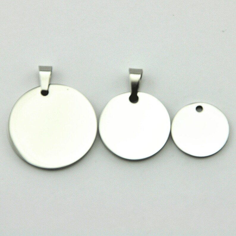 May include: Three silver metal round pendant charms with a loop at the top. The charms are different sizes, with the largest charm being in the center.