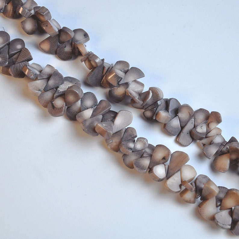 May include: Two strands of a necklace made of small, irregularly shaped, gray-brown beads. The beads have a layered appearance, with lighter and darker shades of gray and brown. The necklace is displayed against a white background.