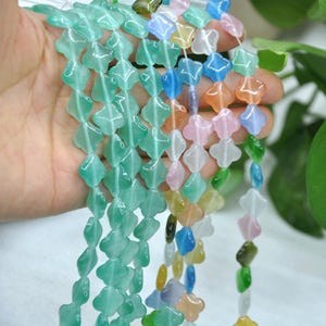 Puede incluir: Hebras de cuentas de piedras preciosas en varios colores, incluyendo verde, azul, rosa y naranja. Las cuentas tienen forma de tr&eacute;boles de cuatro hojas y est&aacute;n ensartadas. Las cuentas se sostienen en una mano.