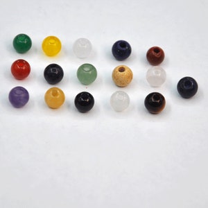 May include: Assortment of 15 round gemstone beads in various colors, including green, yellow, red, purple, blue, brown, black, and white. The beads are arranged in rows on a white surface.