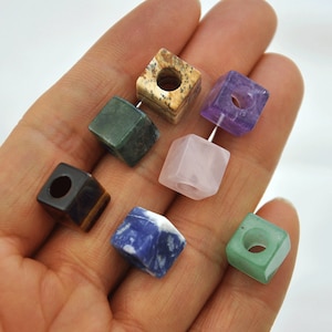 May include: Seven square-shaped gemstone beads with holes in the centre. The beads are in various colours, including green, brown, purple, pink, blue, and light green.