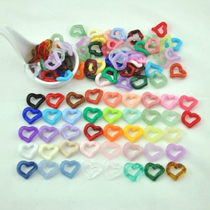 May include: A collection of colorful heart-shaped beads in various shades, including red, blue, green, and yellow. Some beads are in a white spoon. The beads are scattered on a white surface.