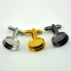 Könnte beinhalten: Drei Manschettenknöpfe mit runden, silbernen, goldenen und schwarzen Metallsockeln. Jeder Manschettenknopf hat einen silbernen, goldenen oder schwarzen Metallsockel mit einem runden, klaren Glaseinsatz.