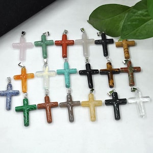 May include: A selection of gemstone cross pendants in a variety of colours, such as pink, green, red, white, black, and brown. Each cross features a silver-coloured bail for attaching to a chain. The crosses are made from different types of stone.