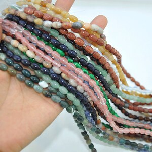 Pu&ograve; includere: Una variet&agrave; di perline di pietre preziose di forma ovale in vari colori, tra cui verde, blu, rosa e marrone. Le perline sono infilate su una corda e sono pronte per la creazione di gioielli.