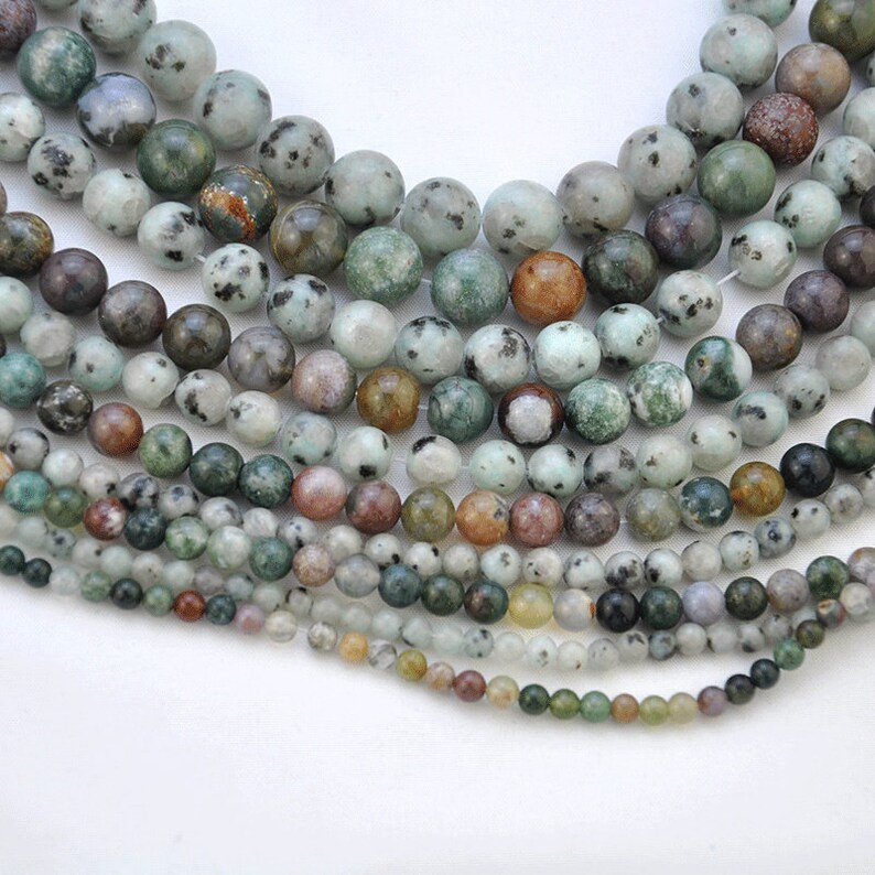 Puede incluir: Una hebra de cuentas de piedra preciosa moteadas de verde, marr&oacute;n y blanco. Las cuentas son redondas y tienen un acabado liso y pulido.