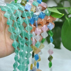 Puede incluir: Hebras de cuentas de piedras preciosas coloridas y transl&uacute;cidas en varias formas y colores, incluyendo verde, azul, rosa y amarillo. Las cuentas se sostienen en una mano, mostrando sus superficies pulidas y dise&ntilde;os &uacute;nicos. Ideal para la fabricaci&oacute;n de joyas.