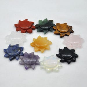 Może przedstawiać: Dziesięć słonecznych zawieszek z kryształu w różnych kolorach, w tym czerwonym, zielonym, brązowym, białym, niebieskim, fioletowym, pomarańczowym i czarnym. Zawieszki są wykonane z polerowanego kamienia i mają gładkie, błyszczące wykończenie.