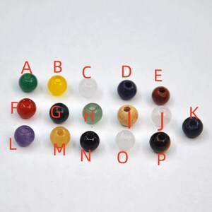 May include: Assortment of 14 round gemstone beads in various colors, including green, yellow, white, blue, red, black, and purple. The beads are labeled with letters from A to P.
