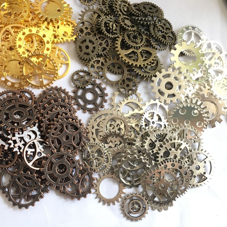 Puede incluir: Una colecci&oacute;n de engranajes de metal dorado, plateado y bronce de varios tama&ntilde;os. Los engranajes est&aacute;n dispuestos en un patr&oacute;n aleatorio sobre un fondo blanco.