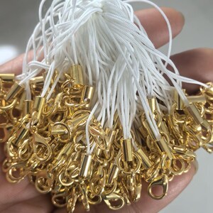 May include: A bunch of white string cords with gold metal clasps and beads. The cords are tied together at the top and the clasps are at the bottom.