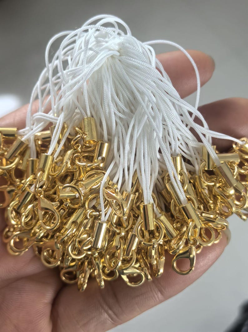 May include: A bunch of white string cords with gold metal clasps and beads. The cords are tied together at the top and the clasps are at the bottom.
