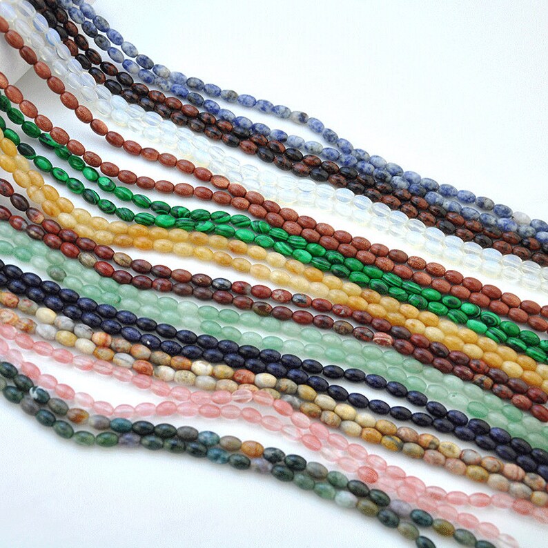 Pu&ograve; includere: Una variet&agrave; di perline ovali in pietre preziose di diversi colori, tra cui verde, blu, rosso, marrone e bianco. Le perline sono infilate su uno spago e sono disposte in file.