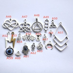 Può includere: Assortimento di ciondoli in argento con vari design, tra cui cuori, simboli dell'infinito, un fulmine, una mano, un occhio, una bandiera da corsa, un simbolo yin yang e un triangolo. I ciondoli sono etichettati con lettere e numeri.