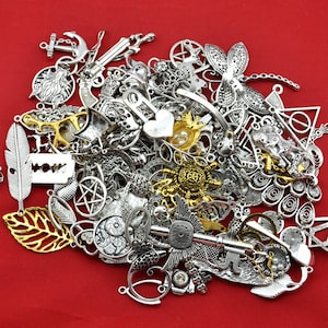 May include: A large assortment of silver and gold metal charms, including keys, anchors, hearts, stars, feathers, and other decorative shapes. The charms are scattered on a red background.
