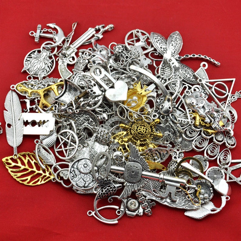 May include: A large assortment of silver and gold metal charms, including keys, anchors, hearts, stars, feathers, and other decorative shapes. The charms are scattered on a red background.