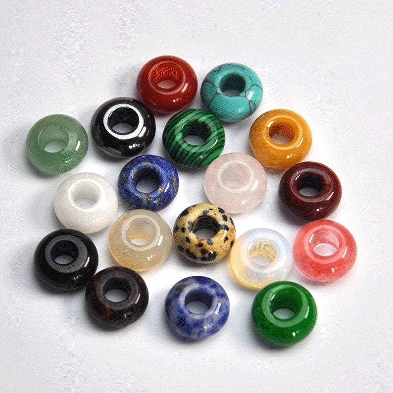 May include: Assortment of 16 gemstone donut beads with various colors and patterns. The beads are made of natural stones and have a hole in the center for stringing.