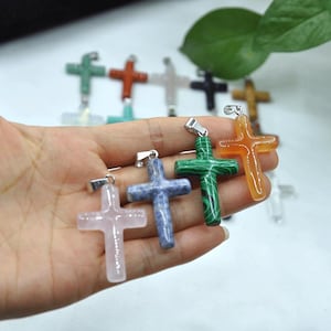 May include: A selection of gemstone cross pendants in shades of pink, blue, green, and orange. Each cross features a silver-coloured bail for attaching to a chain. The crosses are crafted from polished stone.