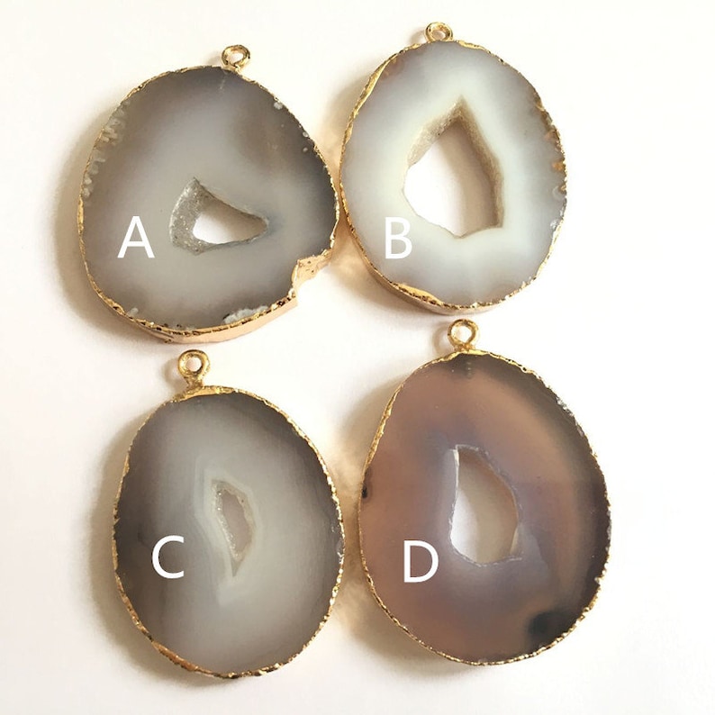 May include: Four agate slices with gold-plated edges and a hole for hanging. The slices are in various shades of gray and white, with a natural hole in the center of each. The slices are labeled A, B, C, and D.
