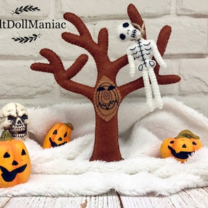 Puede incluir: Un árbol de fieltro de Halloween con una cara espeluznante, un esqueleto colgado y tres calabazas. El árbol es marrón y las calabazas son naranjas.