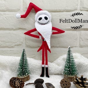 May include: A handmade felt doll of Jack Skellington dressed as Santa Claus. The doll has a white beard and a red Santa hat. The doll is standing in front of a white brick wall. The text "FeltDollManiac" is visible.