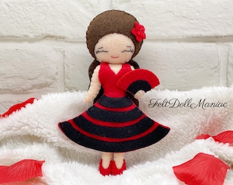 May include: A felt doll dressed in a red and black flamenco dress, holding a black fan. The doll has brown hair and a red flower in her hair. "Felt Doll Maniac" is written on the white background.