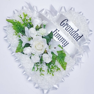 May include: White heart-shaped funeral wreath with white flowers and greenery. A white satin ribbon with the text "Grandad Jimmy" is attached.