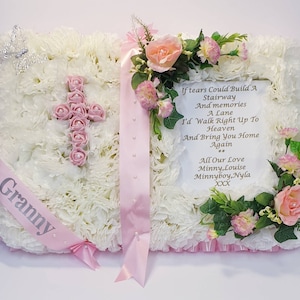 May include: A white and pink floral arrangement in the shape of a book with a pink ribbon and the word "Granny" on it. The arrangement includes a pink cross made of roses and a poem that reads "If tears could build a stairway and memories a lane, I'd walk right up to heaven and bring you home again. All our love, Minny, Louise, Minnyboy, Nyla XXX."