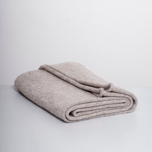 May include: A folded beige knitted throw blanket.