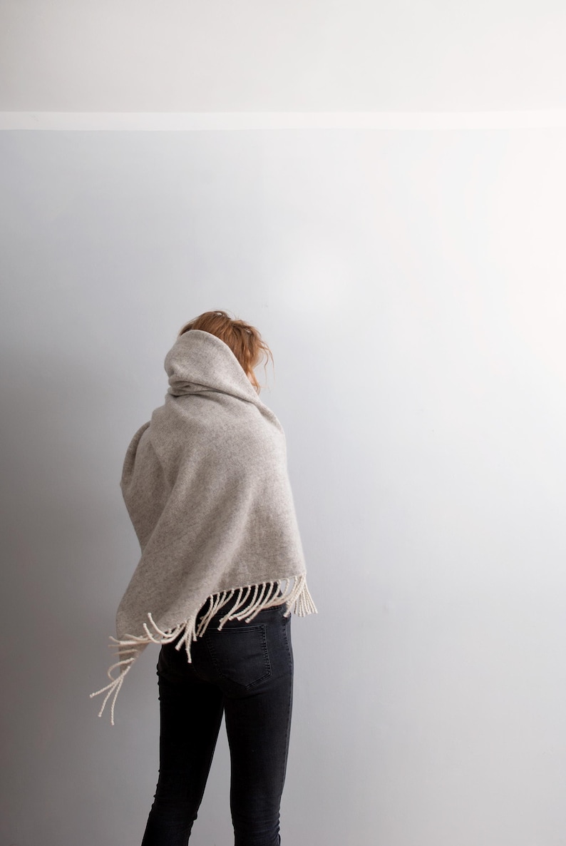 Back view of a woman wearing a thick beige wool blanket shawl wrapped over her head and shoulders.