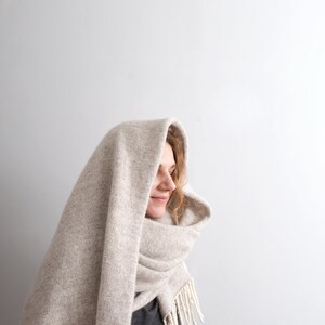 Profile of a smiling woman wearing a cozy beige melange mohair wool blanket scarf wrapped around her head.