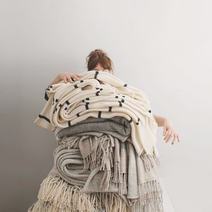May include: A stack of white and grey blankets with black stripes and fringe. The blankets are folded and piled on top of each other.