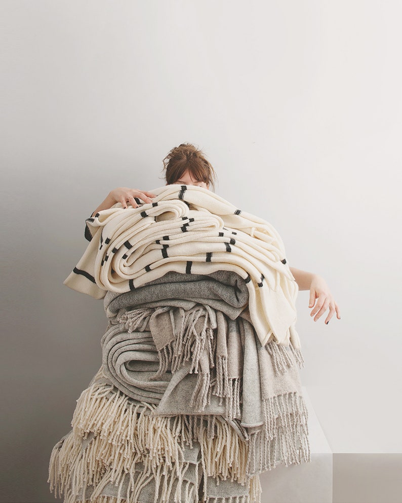 May include: A stack of white and grey blankets with black stripes and fringe. The blankets are folded and piled on top of each other.