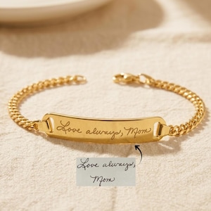 Peut inclure: Un bracelet à chaîne en métal doré doté d'une plaque d'identification rectangulaire centrale. La plaque est gravée avec le texte en écriture cursive "Love always, Mom", correspondant à la note manuscrite visible sous le bracelet.