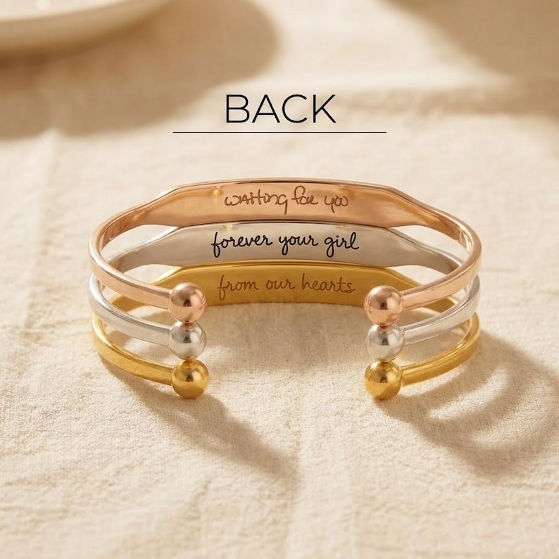 May include: A set of three open cuff bracelets in rose gold, silver, and gold tones. Each bracelet features a spherical end and an engraved inscription. The top reads 'waiting for you', the middle 'forever your girl', and the bottom 'from our hearts'.