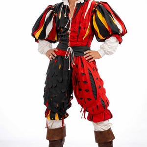 Könnte beinhalten: Ein Renaissance-Kostüm in Rot, Schwarz, Gelb und Weiß. Das Outfit umfasst ein Oberteil mit Puffärmeln, eine Kniebundhose und hohe braune Stiefel. Das Oberteil ist vertikal geteilt, eine Seite schwarz und die andere rot. Die Kniebundhose hat ein einzigartiges Cut-Out-Design.