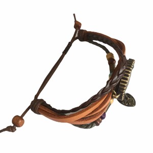 Peut inclure: Un bracelet en cuir marron avec un design tress&eacute; et un charme en m&eacute;tal. Le charme a un motif d'arbre et est attach&eacute; &agrave; une pi&egrave;ce ronde en m&eacute;tal avec une surface textur&eacute;e.