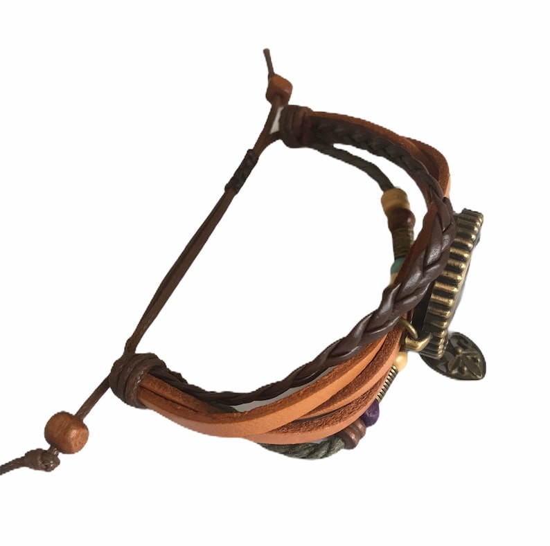 Peut inclure: Un bracelet en cuir marron avec un design tress&eacute; et un charme en m&eacute;tal. Le charme a un motif d'arbre et est attach&eacute; &agrave; une pi&egrave;ce ronde en m&eacute;tal avec une surface textur&eacute;e.
