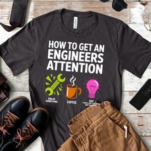 Dark t-shirt with "How to Get an Engineer's Attention" text and icons.
