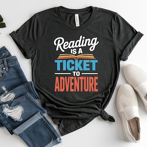 Dark t-shirt with "Reading is a Ticket to Adventure" text and book graphic.