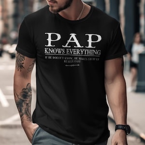 May include: Black t-shirt with the text "PAP KNOWS EVERYTHING" in white, with the additional text "IF HE DOESN'T KNOW, HE MAKES STUFF UP REALLY FAST". The shirt is short-sleeved and has a crew neck.