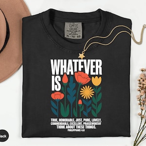 May include: Black t-shirt with the text "WHATEVER IS" above a floral design in red, orange, blue, and yellow. The text "TRUE, HONORABLE...THINK ABOUT THESE THINGS. PHILIPPIANS 4:8" is below the floral design. A gold necklace with a star pendant is on the shirt.