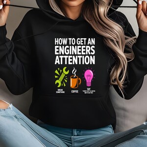 Black hoodie with "How to get an engineers attention" text, coffee, and lightbulb icons.