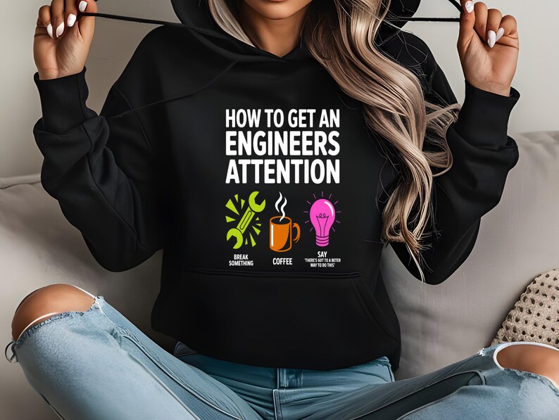 Black hoodie with "How to get an engineers attention" text, coffee, and lightbulb icons.