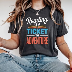 Woman wearing dark t-shirt with "Reading is a Ticket to Adventure" text.