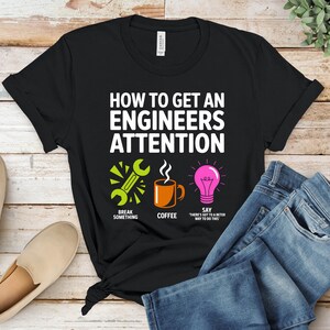 Black t-shirt with "How to Get an Engineer's Attention" and three icons.