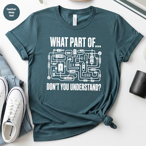 May include: A heather deep teal t-shirt with the text "WHAT PART OF... DON'T YOU UNDERSTAND?" in white. The graphic features a circuit diagram. The shirt is styled with rolled sleeves and a knotted hem.
